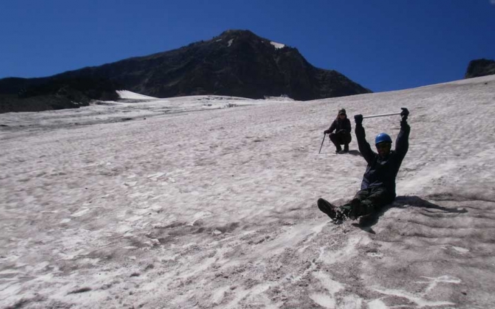 a person raises their hands as they sit and slide down a snowy slope